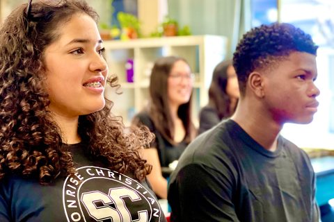 students smiling together while seated at a classroom table, enjoying a lesson